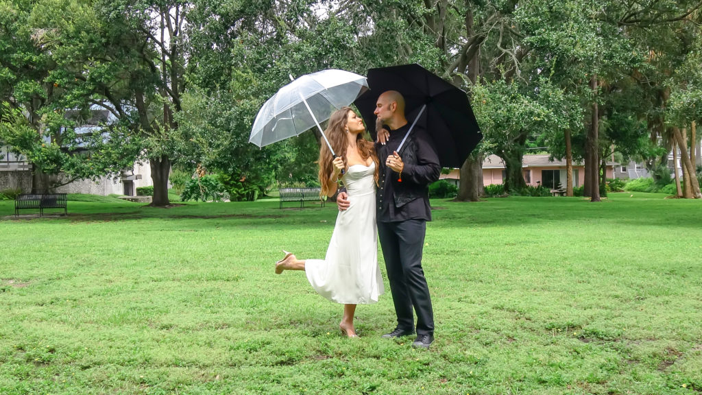 bride and groom with umbrellas in the park