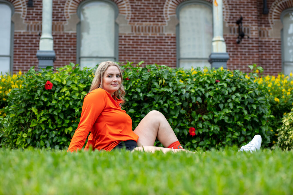 girl in her soccer uniform sitting in the grass in front of a brick building