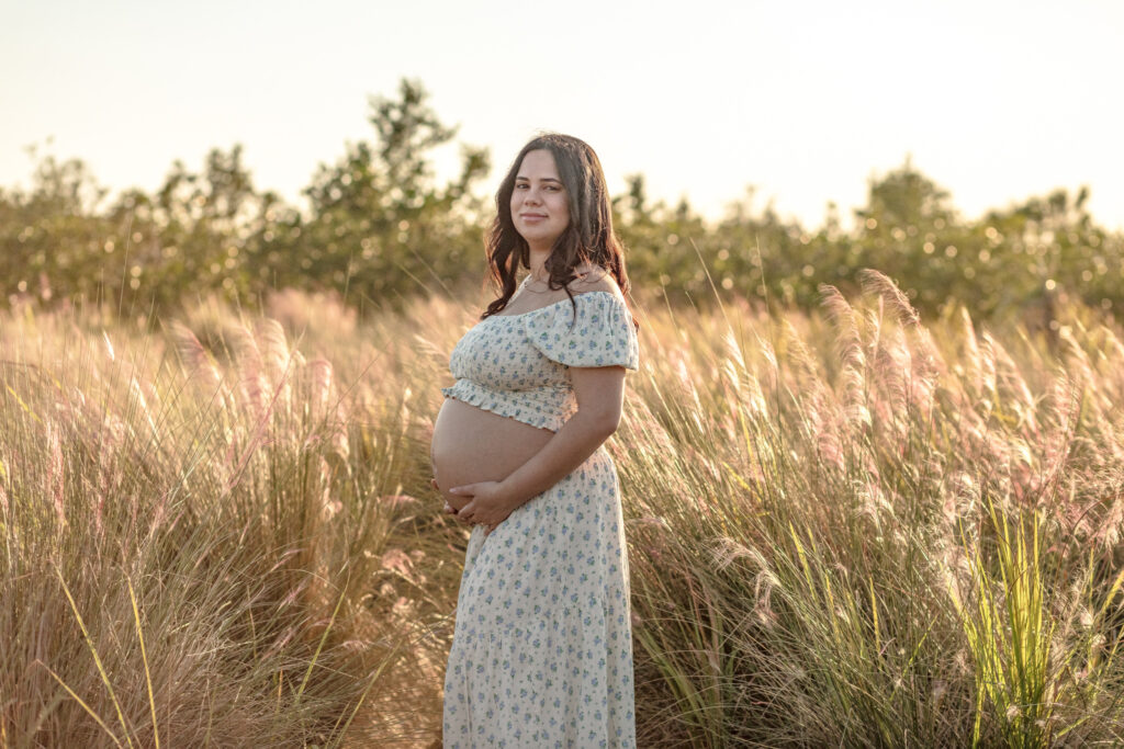 momma holding her pregnant belly in a rustic dress standing in the middle of a wheat field at sunset
