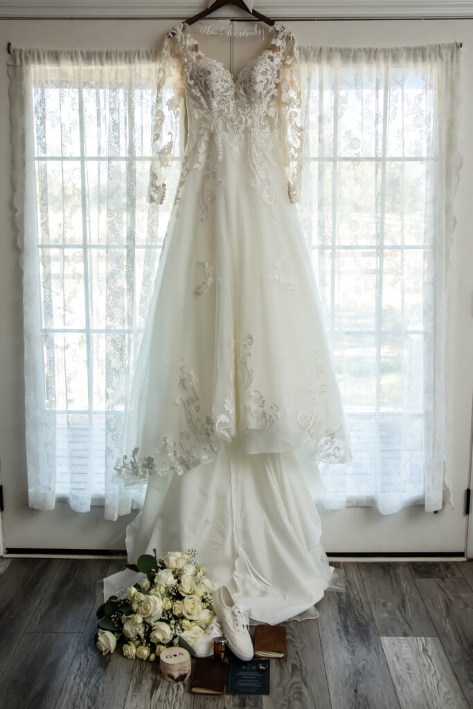 Brides wedding dress hanging in front of double doors with her flowers and shoes