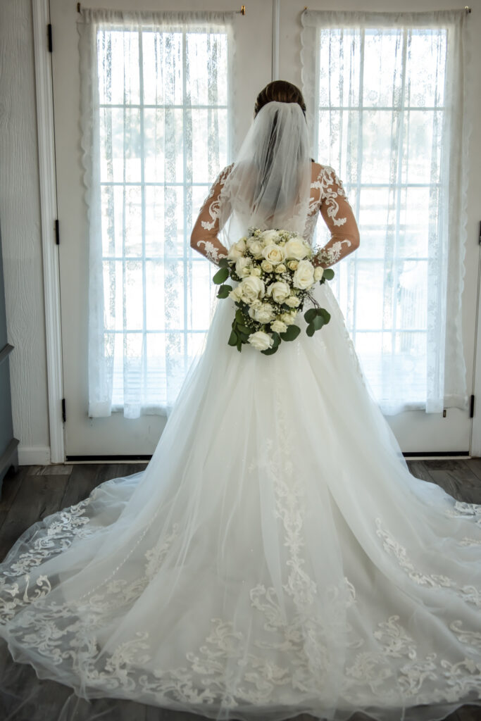 Bride facing double doors holding flowers behind her back