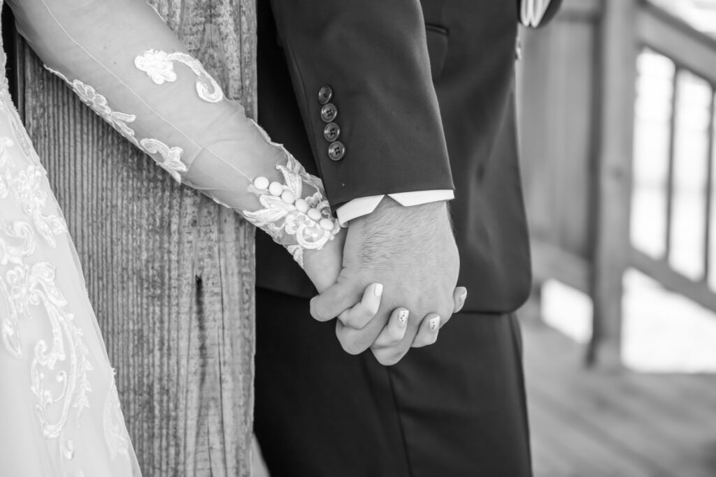 Up close of bride and groom holding hands on the outside of the cottage