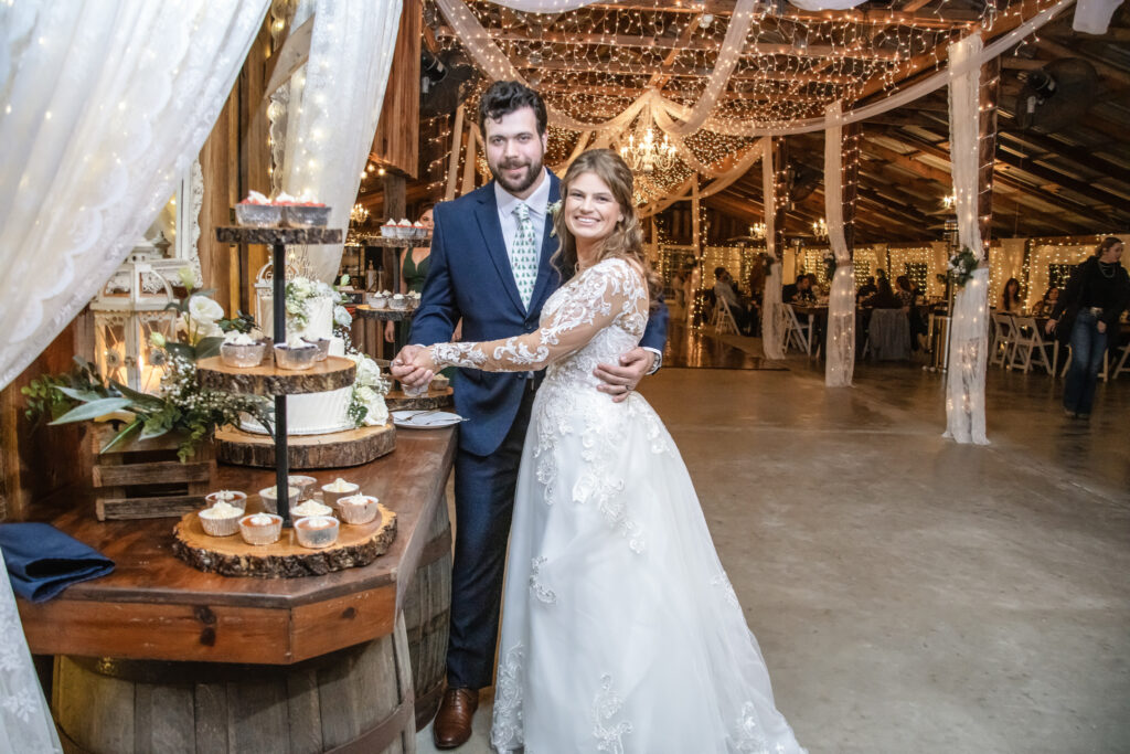 Bride and groom posing with their wedding cake inside a barn
