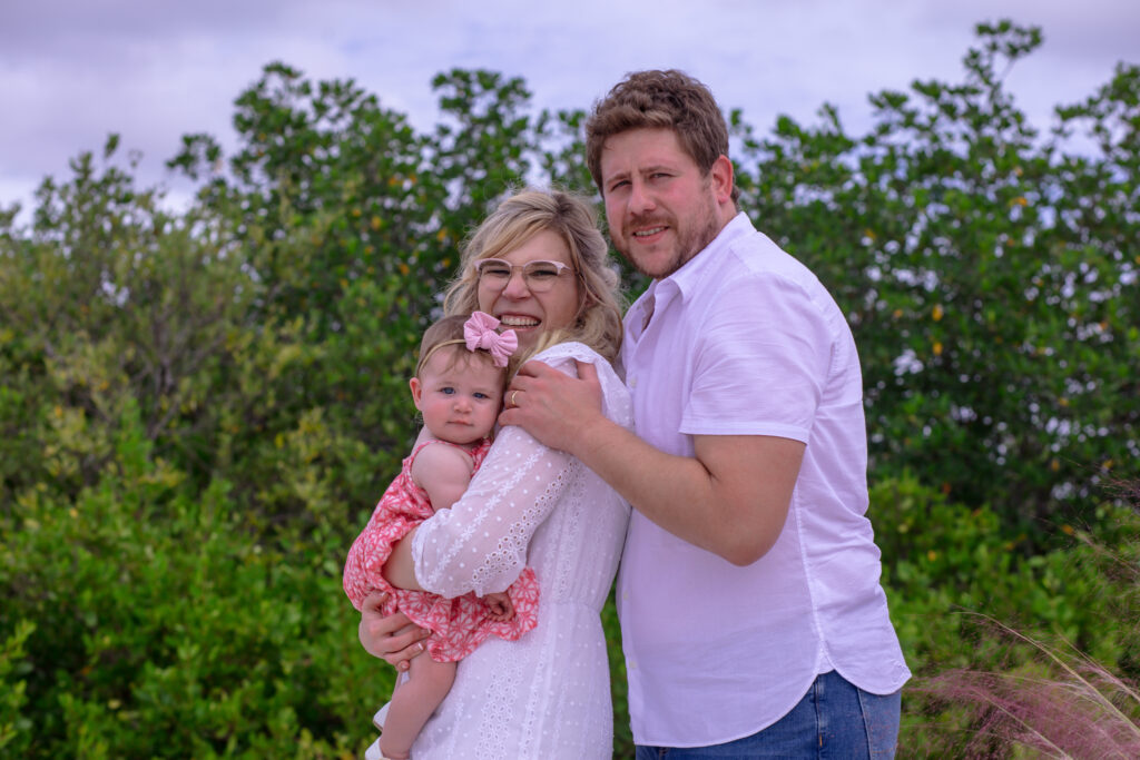 family of three in a grassy area by the beach water at sunset