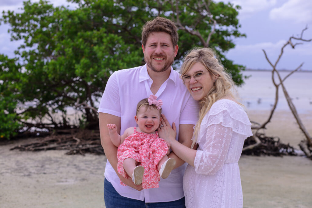 family of three in a grassy area by the beach water at sunset