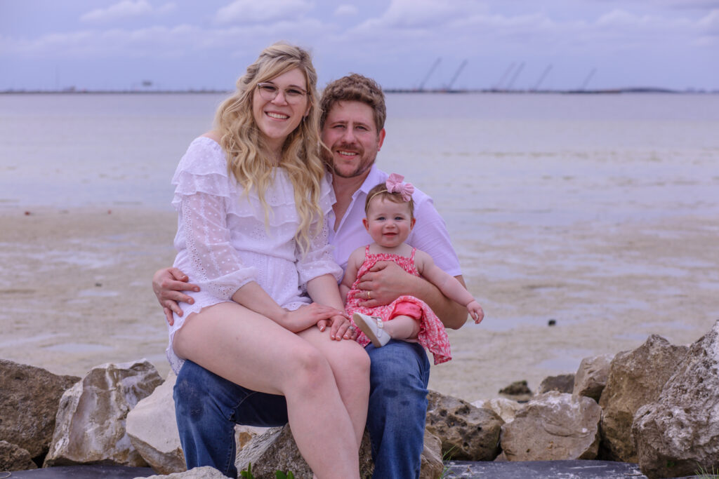 family of three sitting on the rocks at the beach at sunset