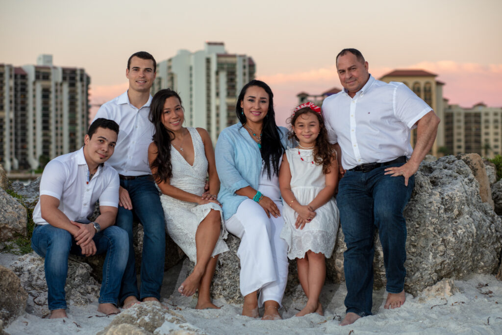 family of 6 sitting on a pile of rocks on the beach at sunset