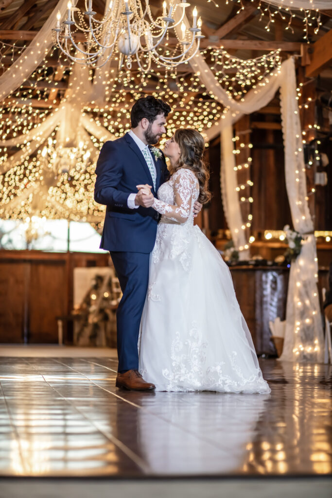 Bride and groom having their first dance under the lights inside a barn