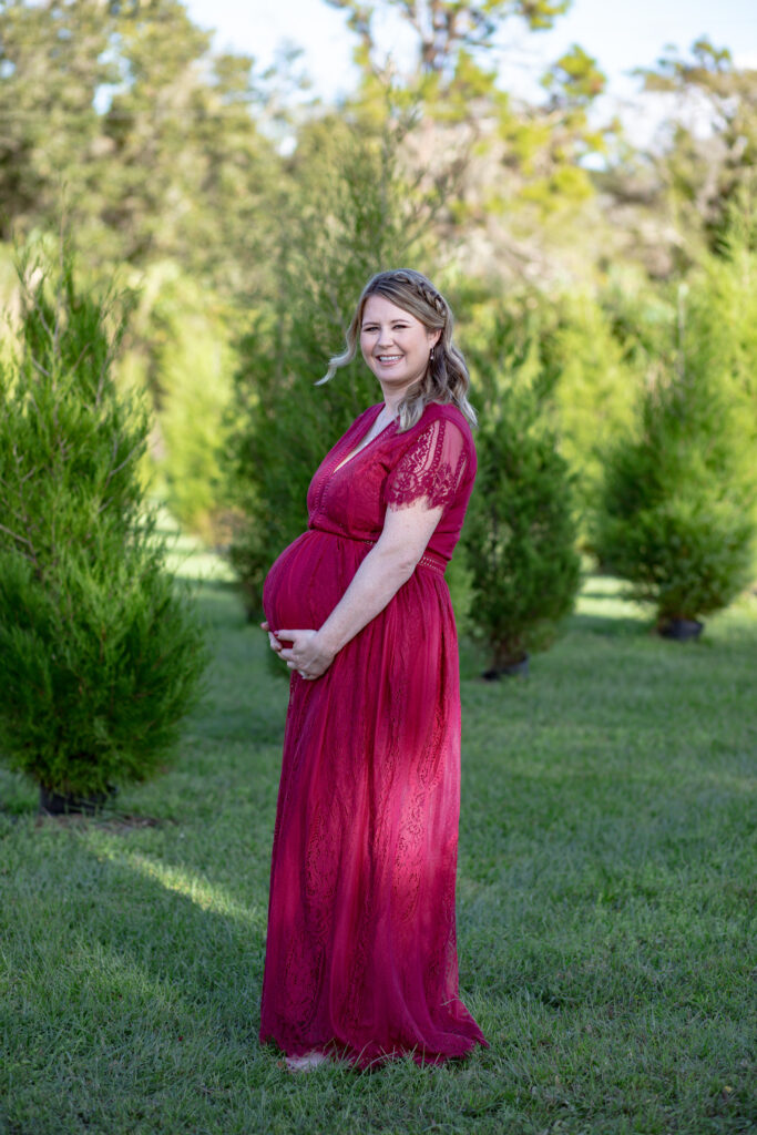 momma holding the bottom of her pregnant belly in a red dress in the vineyards