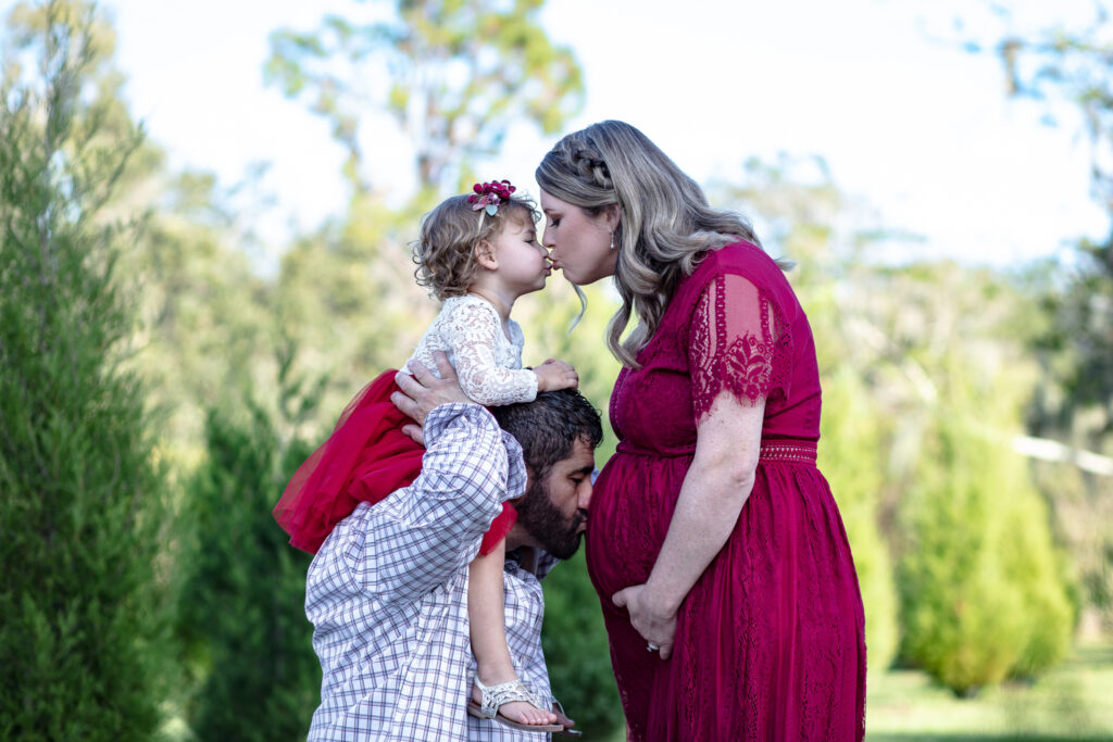 family of three kissing pregnant mommas belly