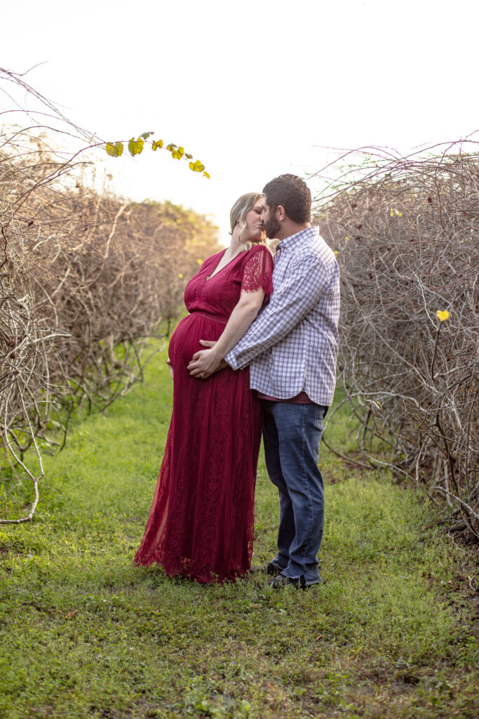 parents holding the belly of the momma in a vineyard