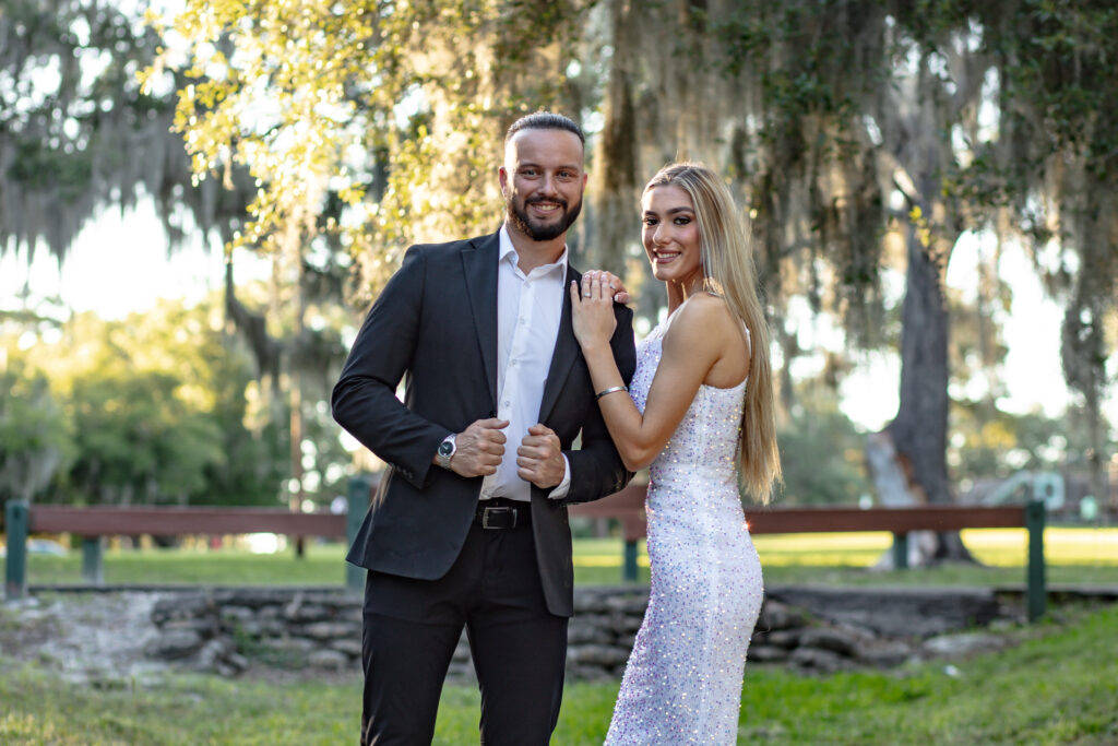 couple posing under a big tree in the grass at a park at sunset