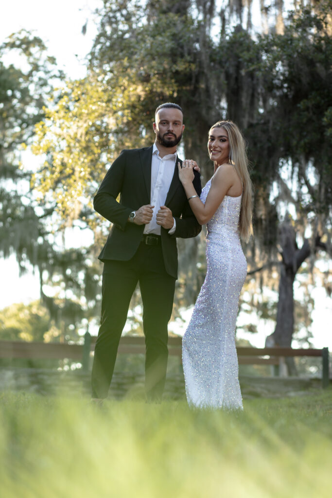 couple posing in the grass under a big tree in the park at sunset