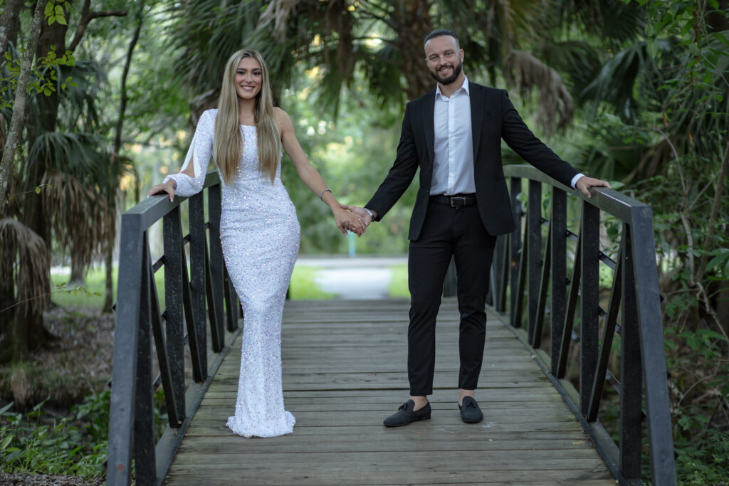 couple holding hands on a bridge in a park surrounded by trees