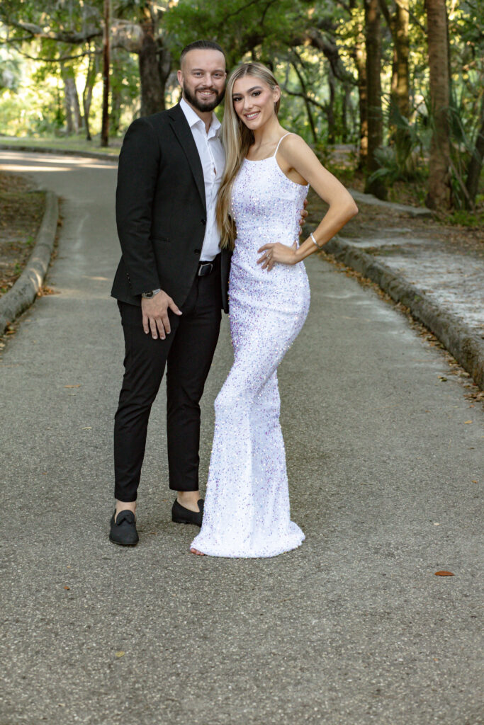 Couple holding each other on a concrete pathway in park at sunset surrounded by trees