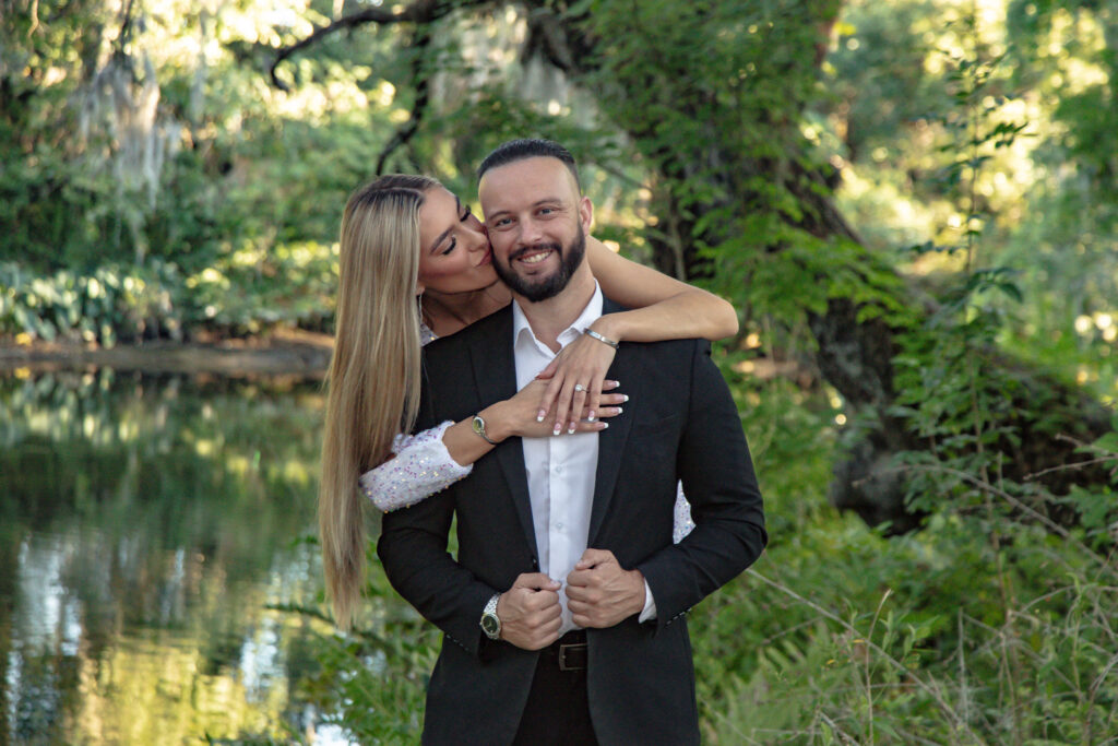 couple sharing a kiss with the women standing behind the man with the river behind them