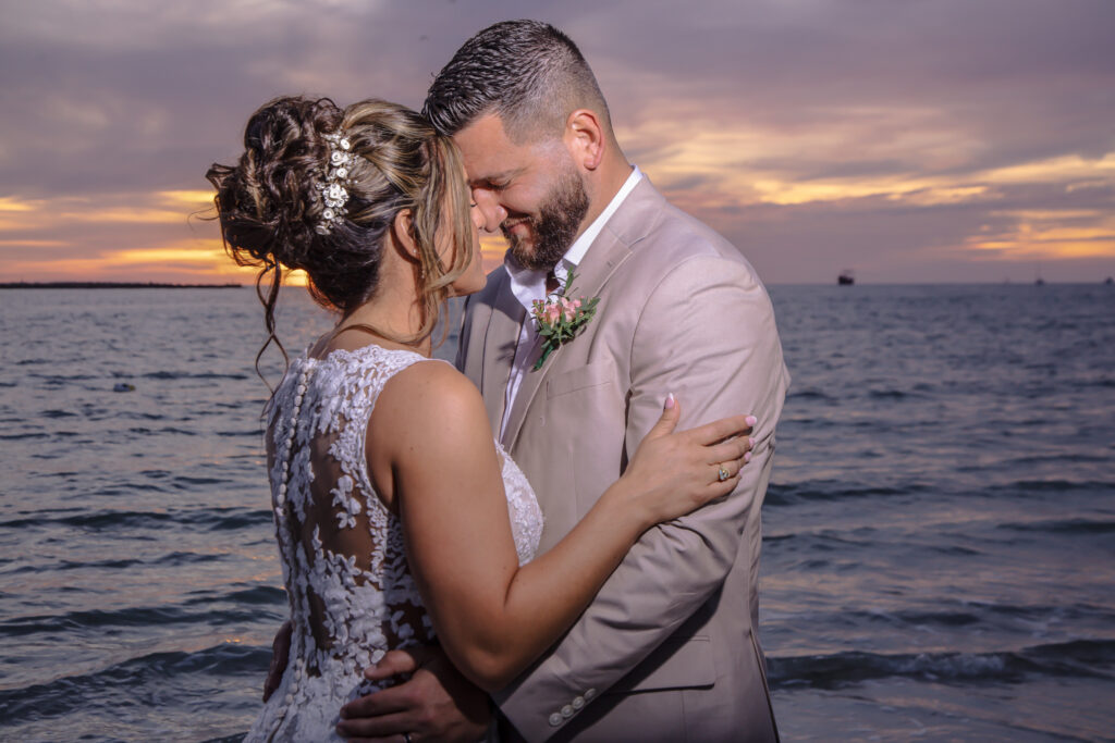 bride and groom with their heads together on the beach at sunset