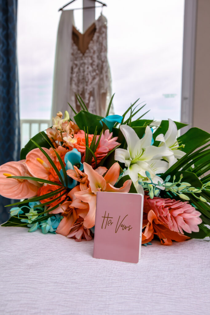brides vow book in front of her flowers with dress hanging in the background