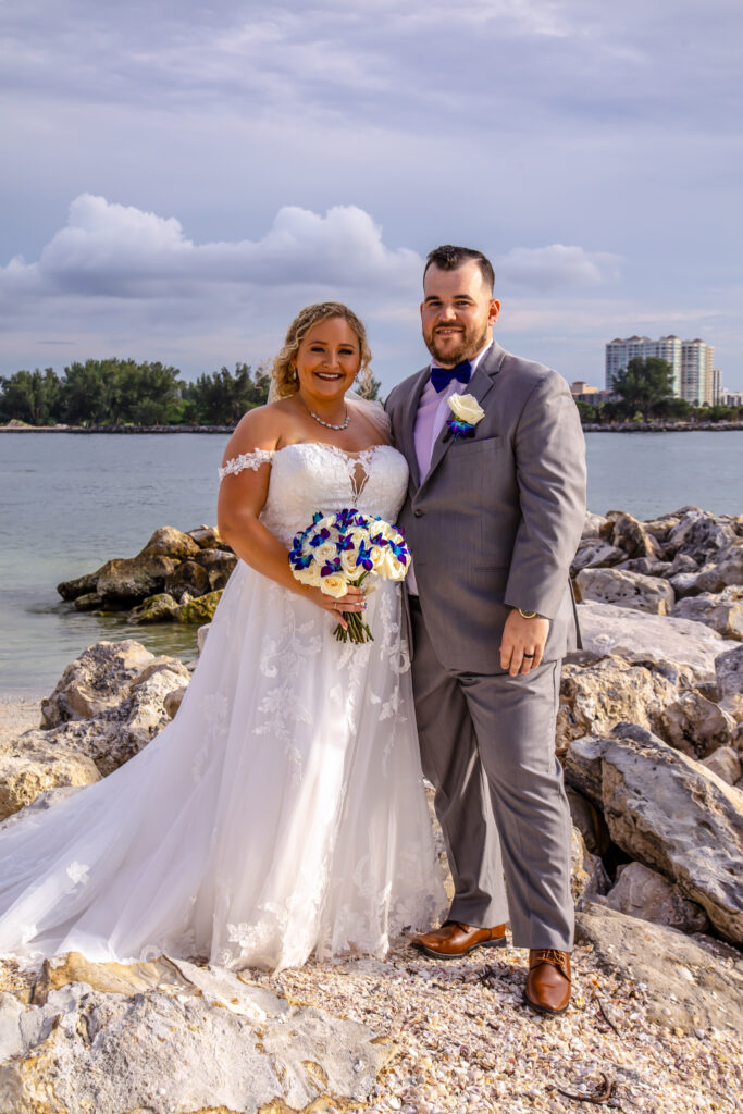 bride and groom standing on the beach by some rocks
