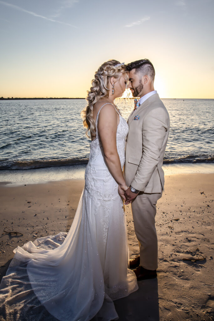 bride and grooms with their heads together, standing on the beach at sunset