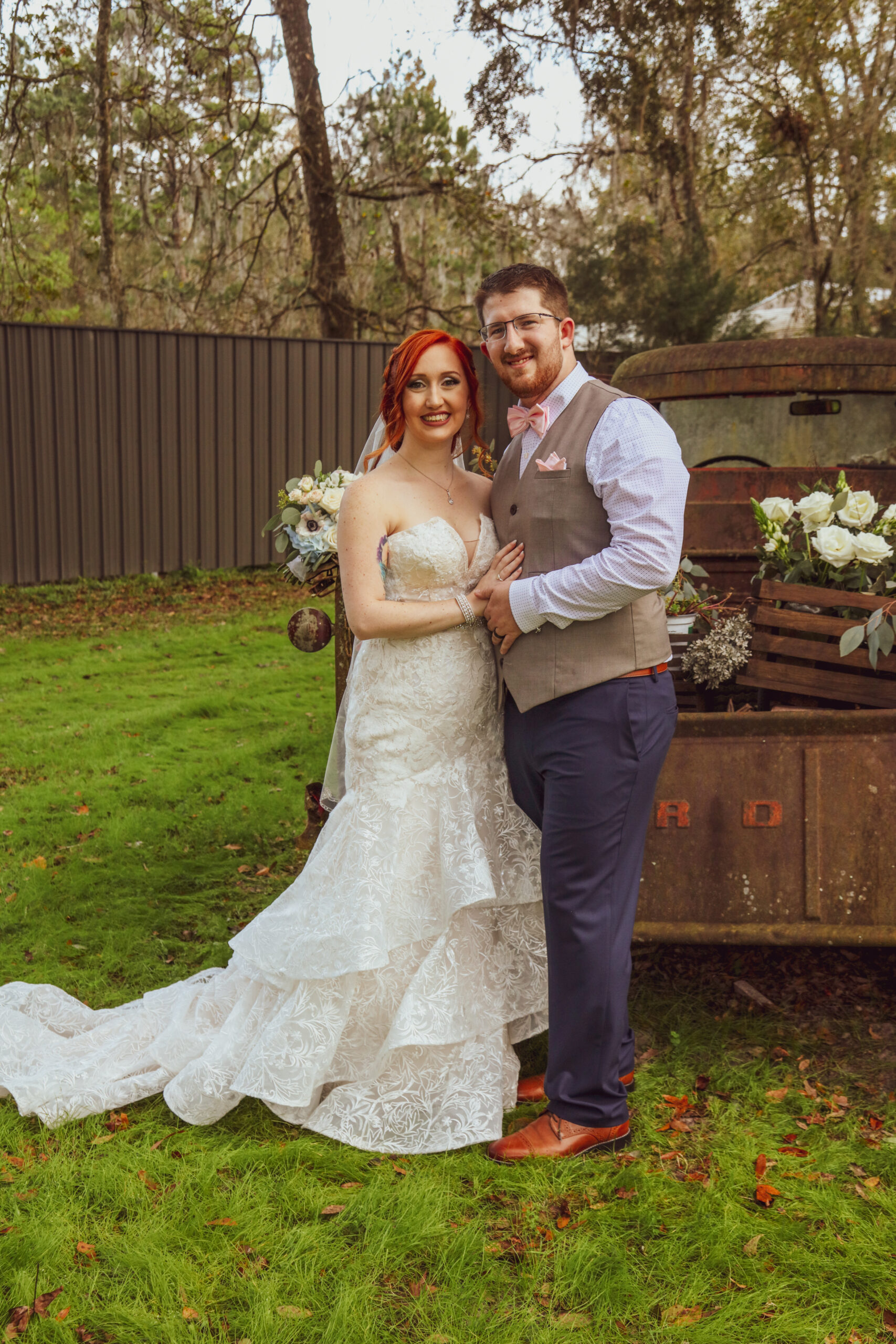 bride and groom posing behind a rusty old truck