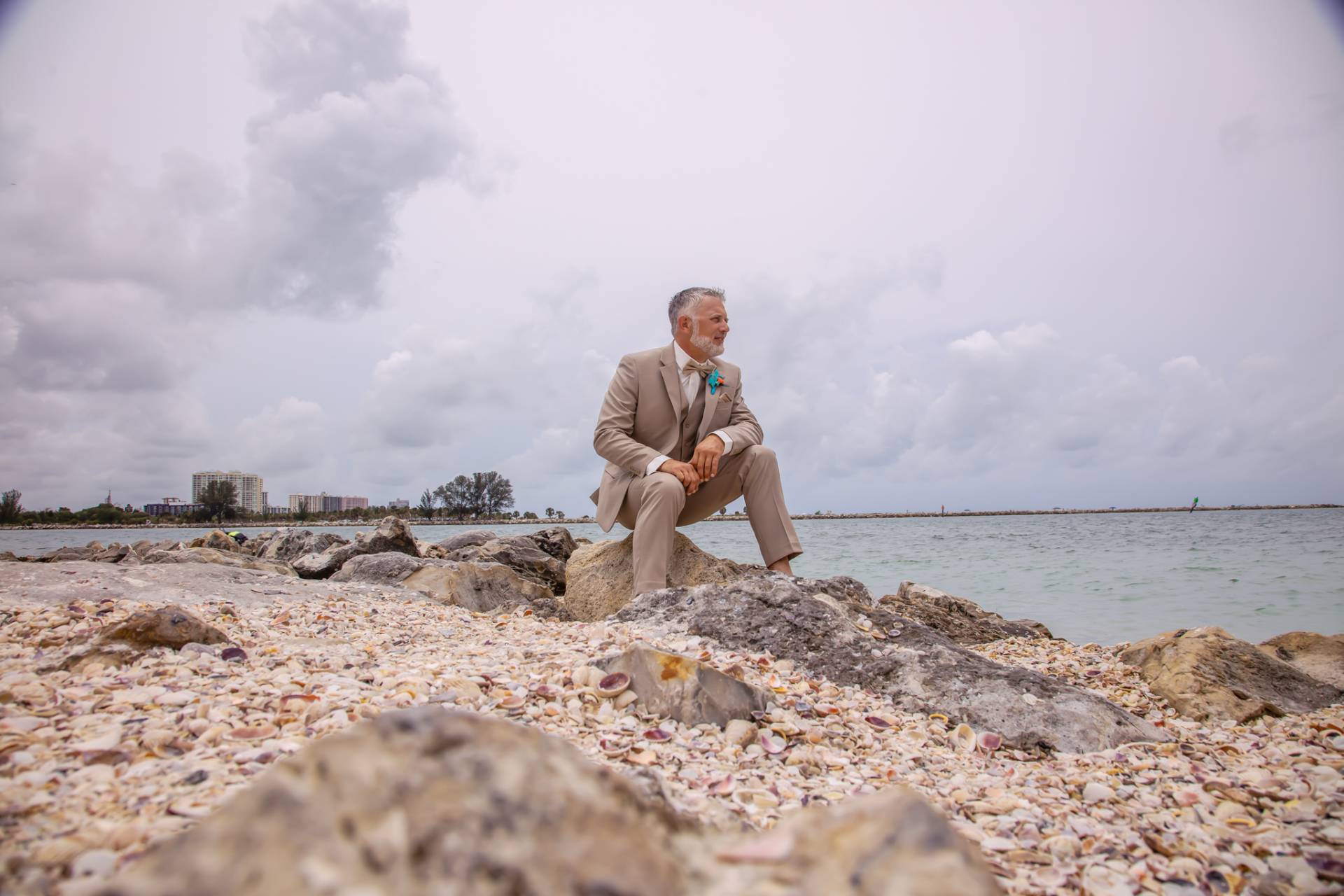 groom sitting on some rocks on the beach