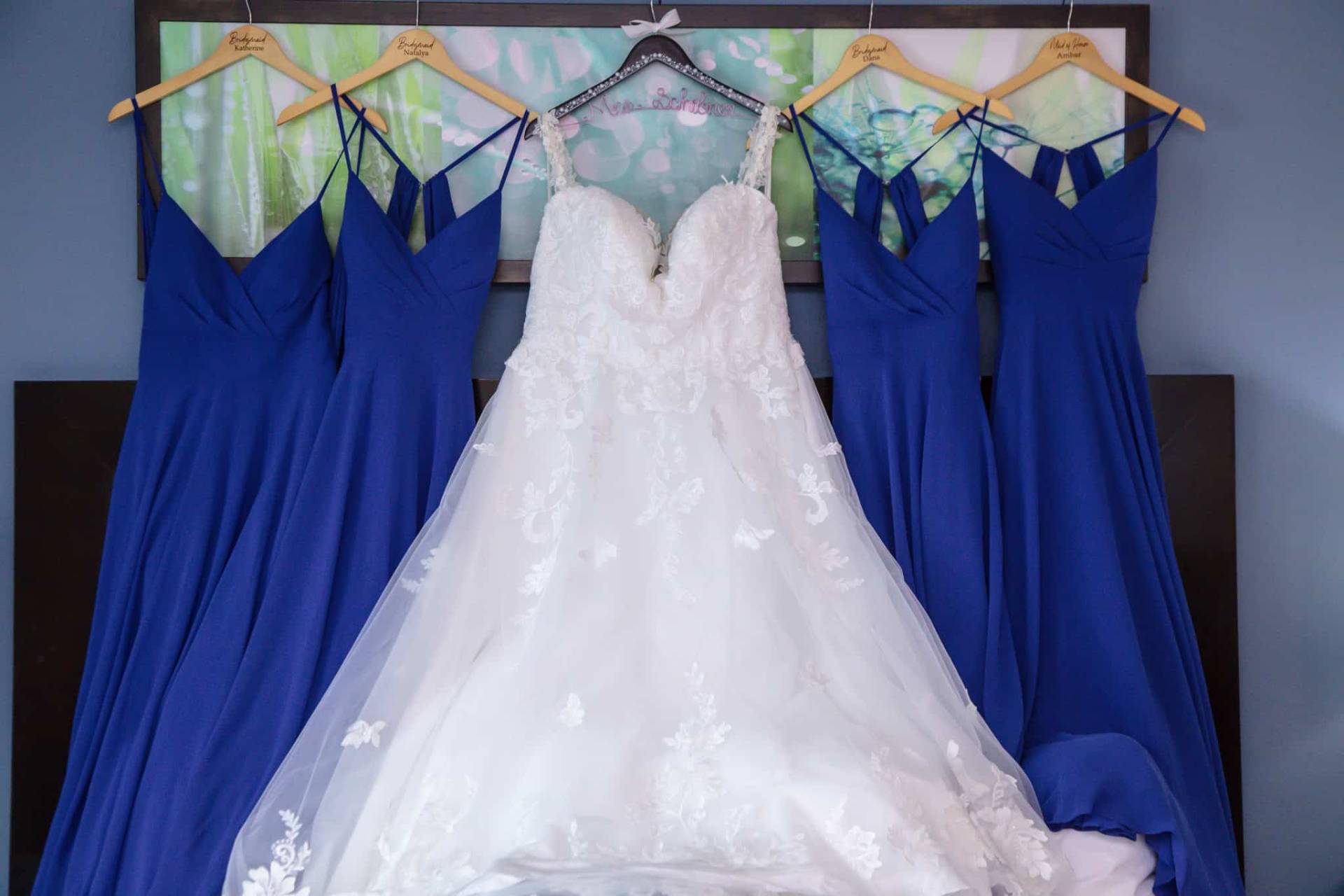 brides dress hanging with bridesmaids dresses above the bed