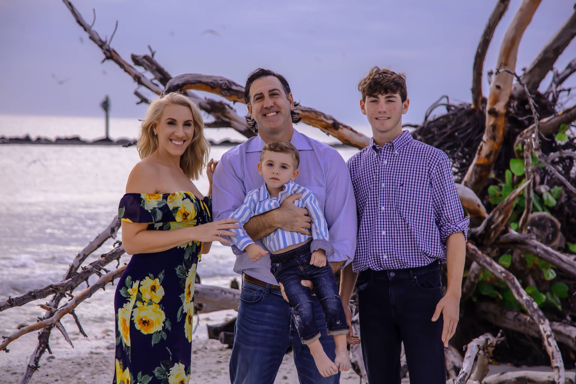 family of four on the beach standing in front of a fallen tree