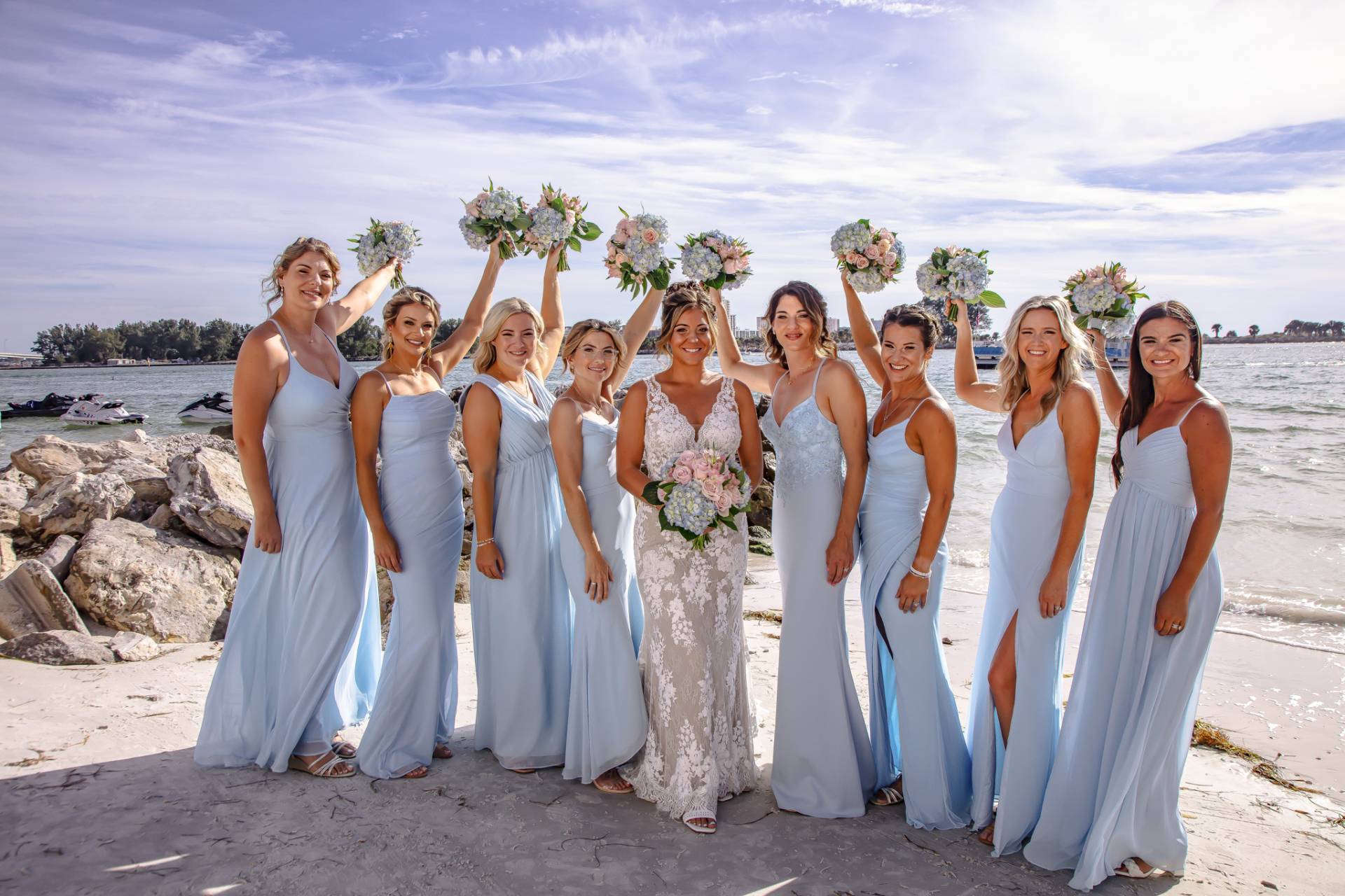 bride with her bridesmaids and their flowers on the beach near some rocks
