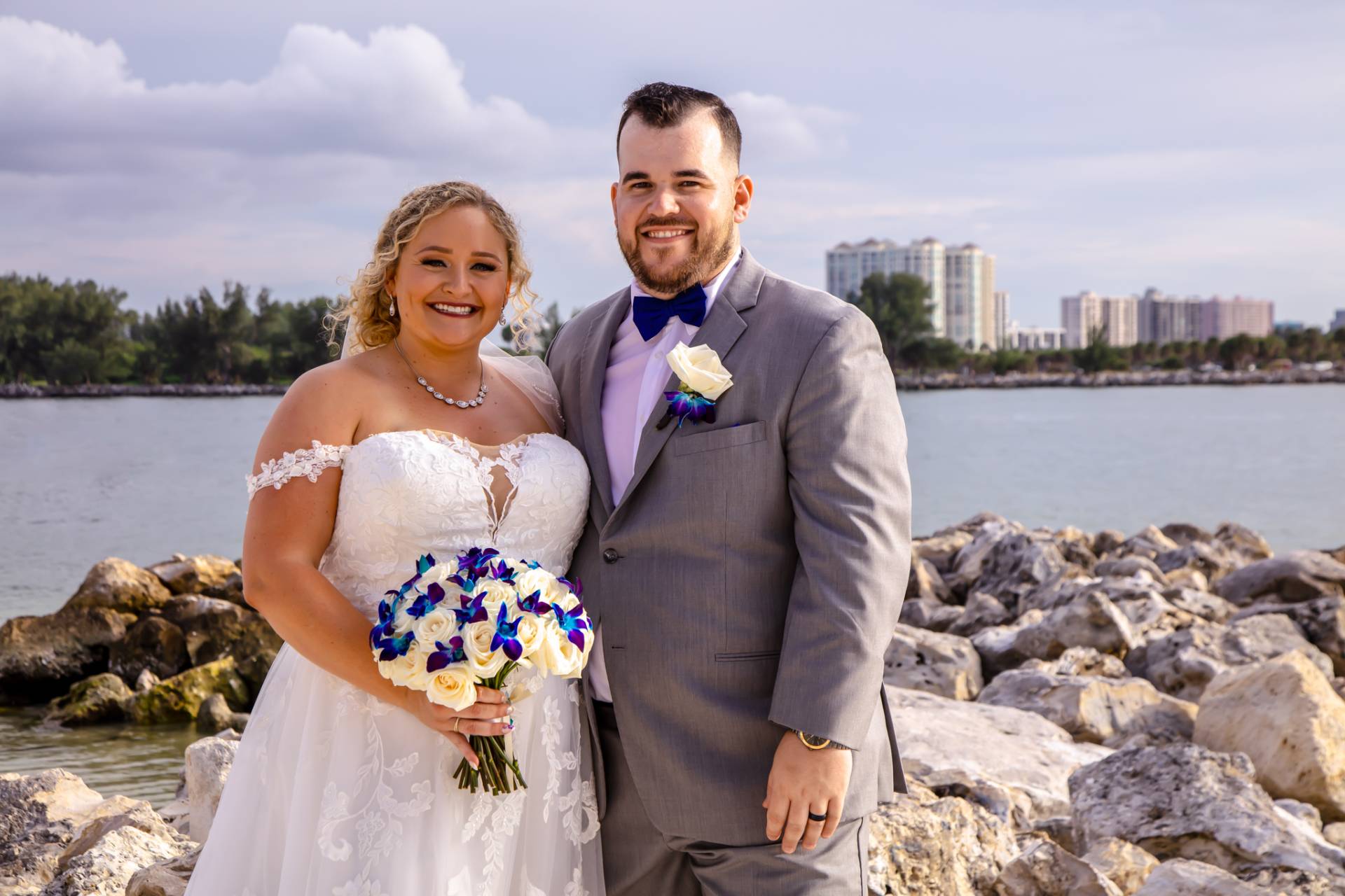 bride and groom standing on the beach by some rocks