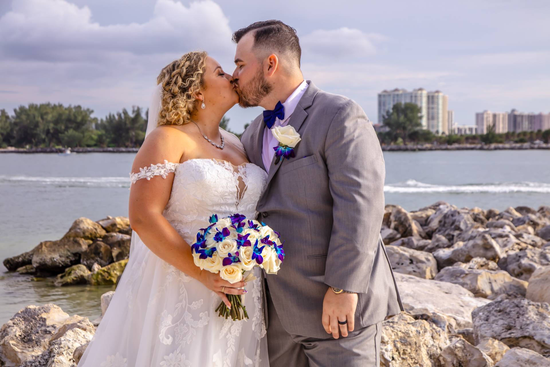 bride and groom kissing on the beach, standing on some rocks
