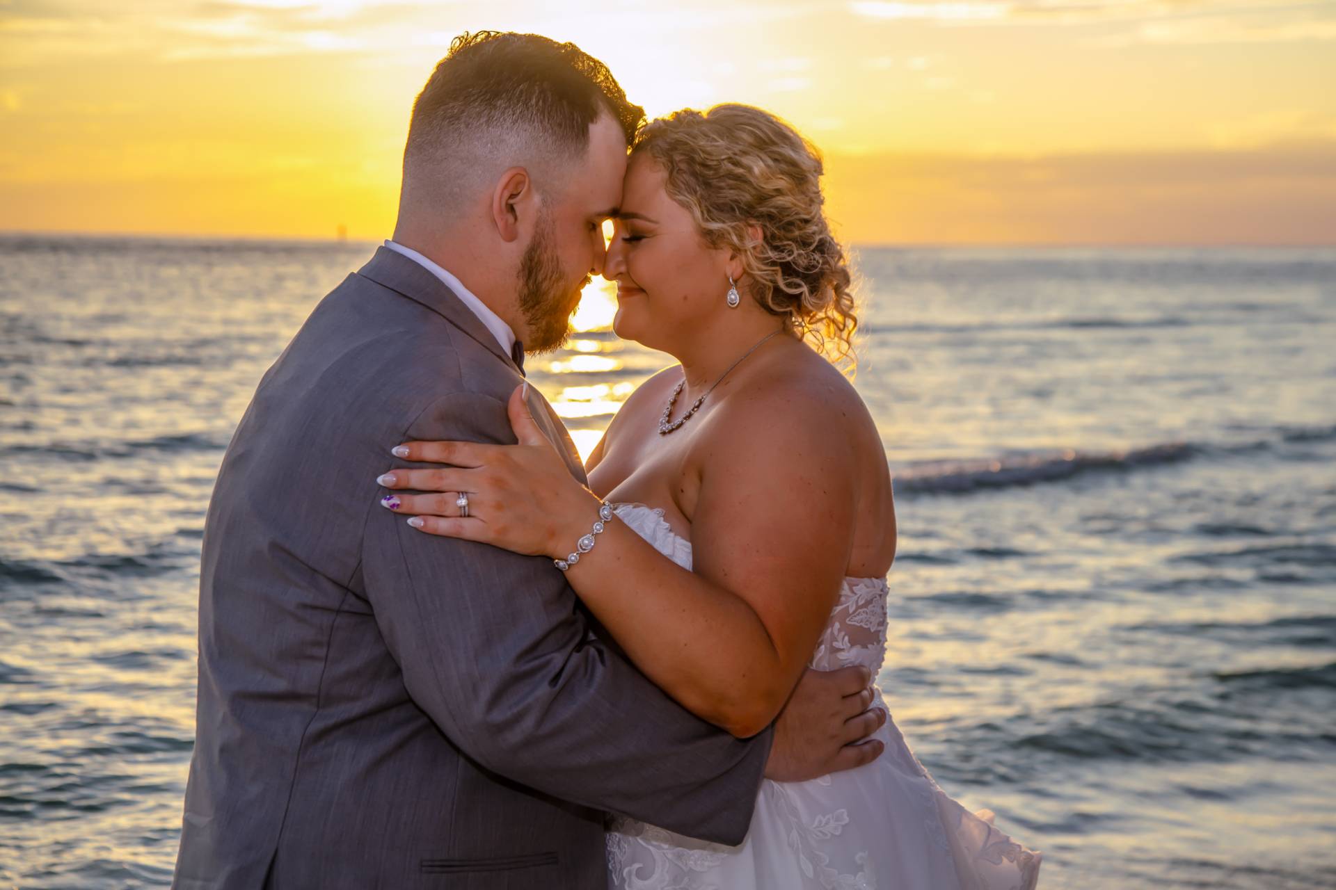 bride and groom with their heads together on the beach at sunset