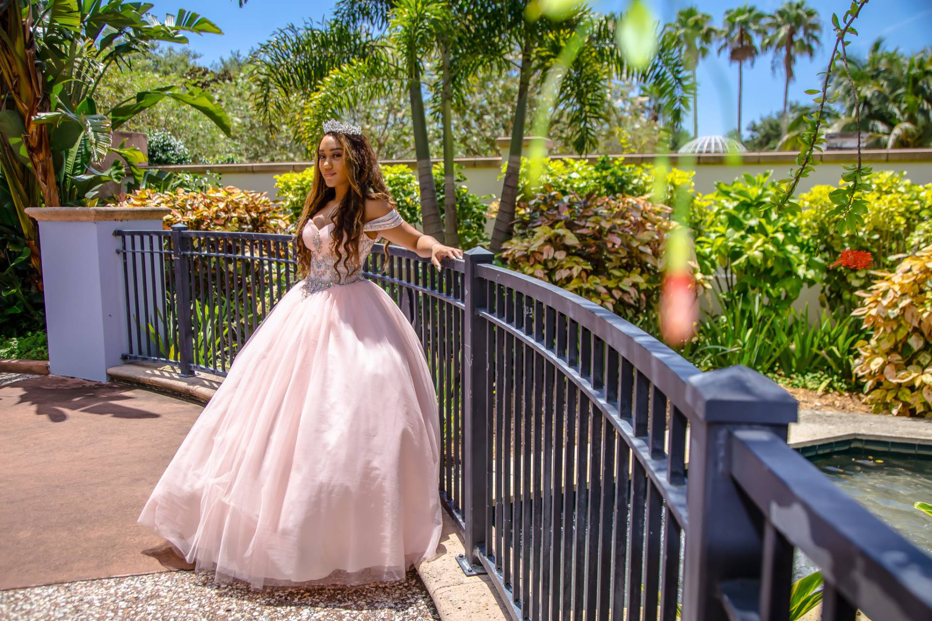 Quinceanera girl in her pink dress standing against a black iron fence