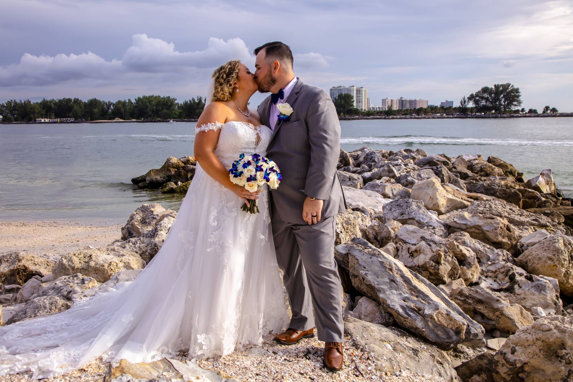 bride and groom kissing on the beach, standing on some rocks