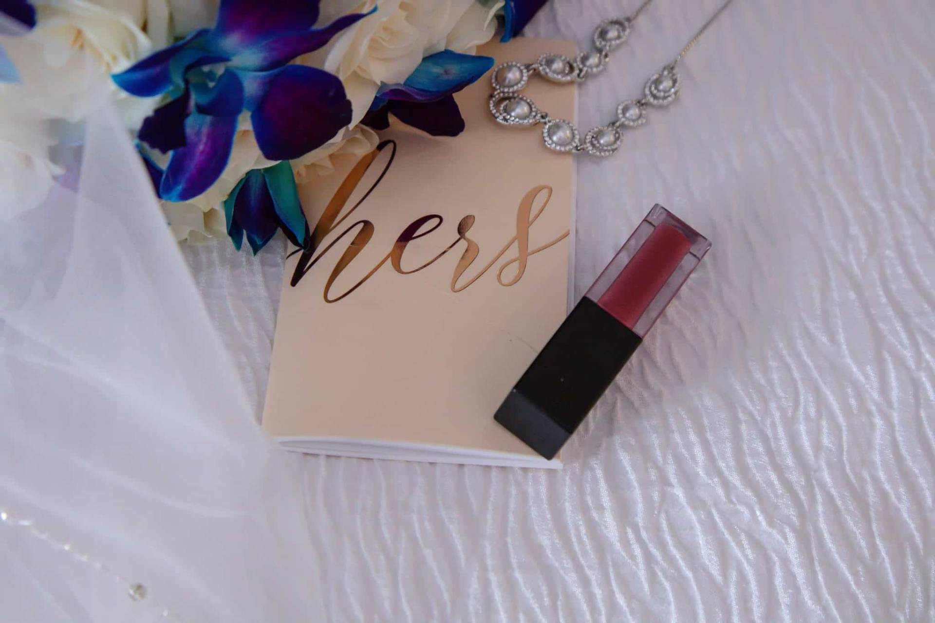 brides vow book with lipstick, jewelry, flowers, and veil