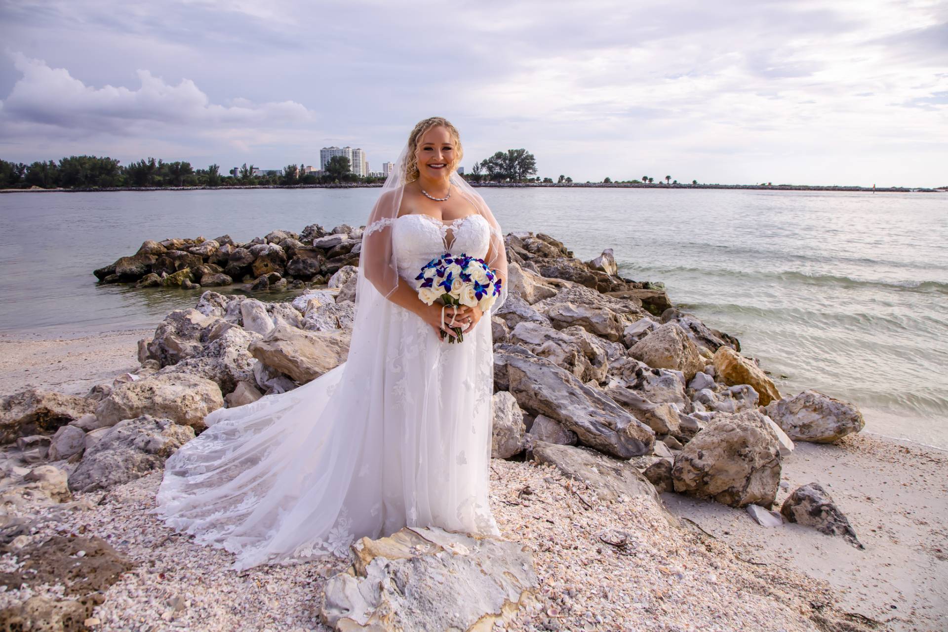 bride standing on some rocks on the beach in her wedding dress