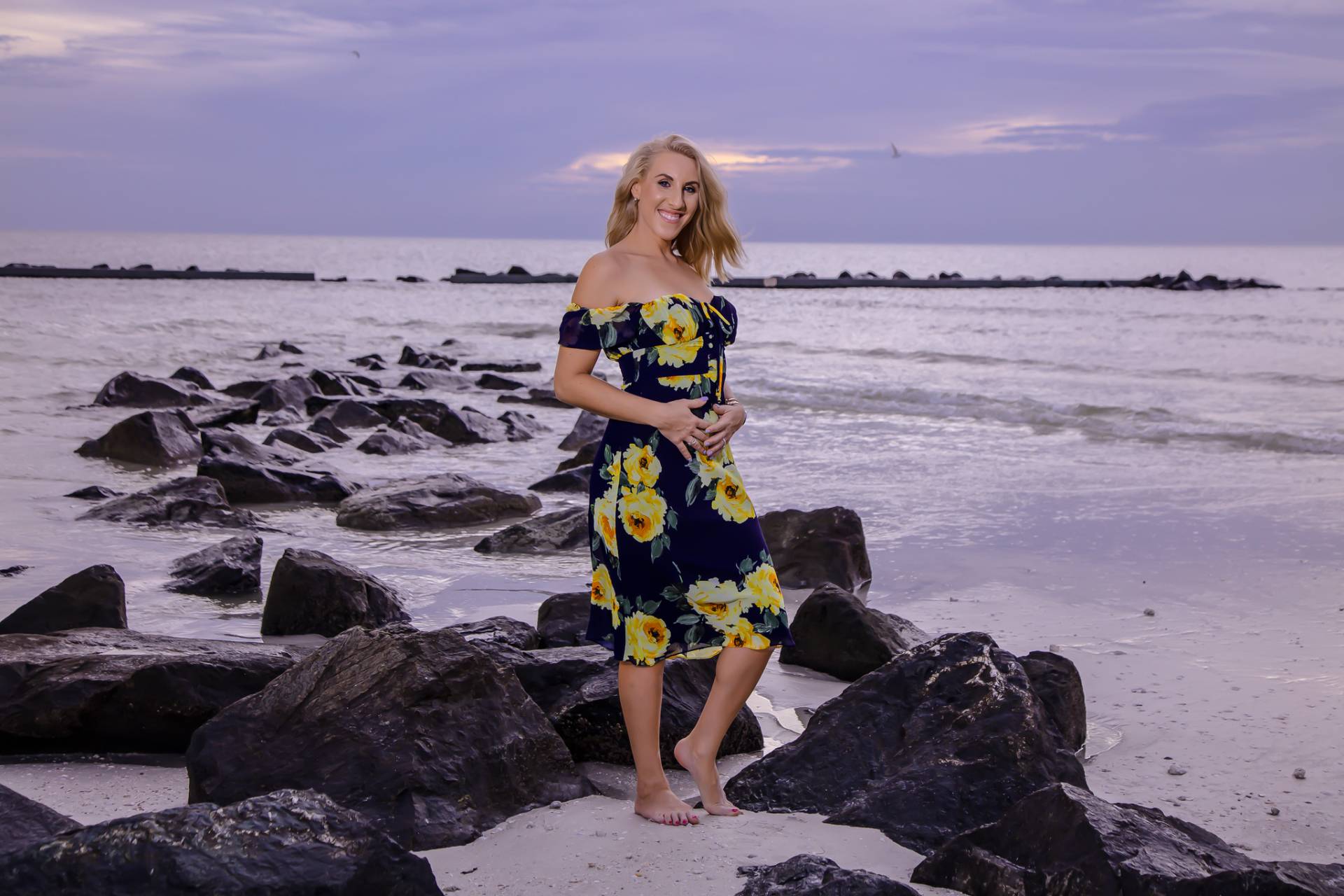 female standing on black rocks on the beach in the water