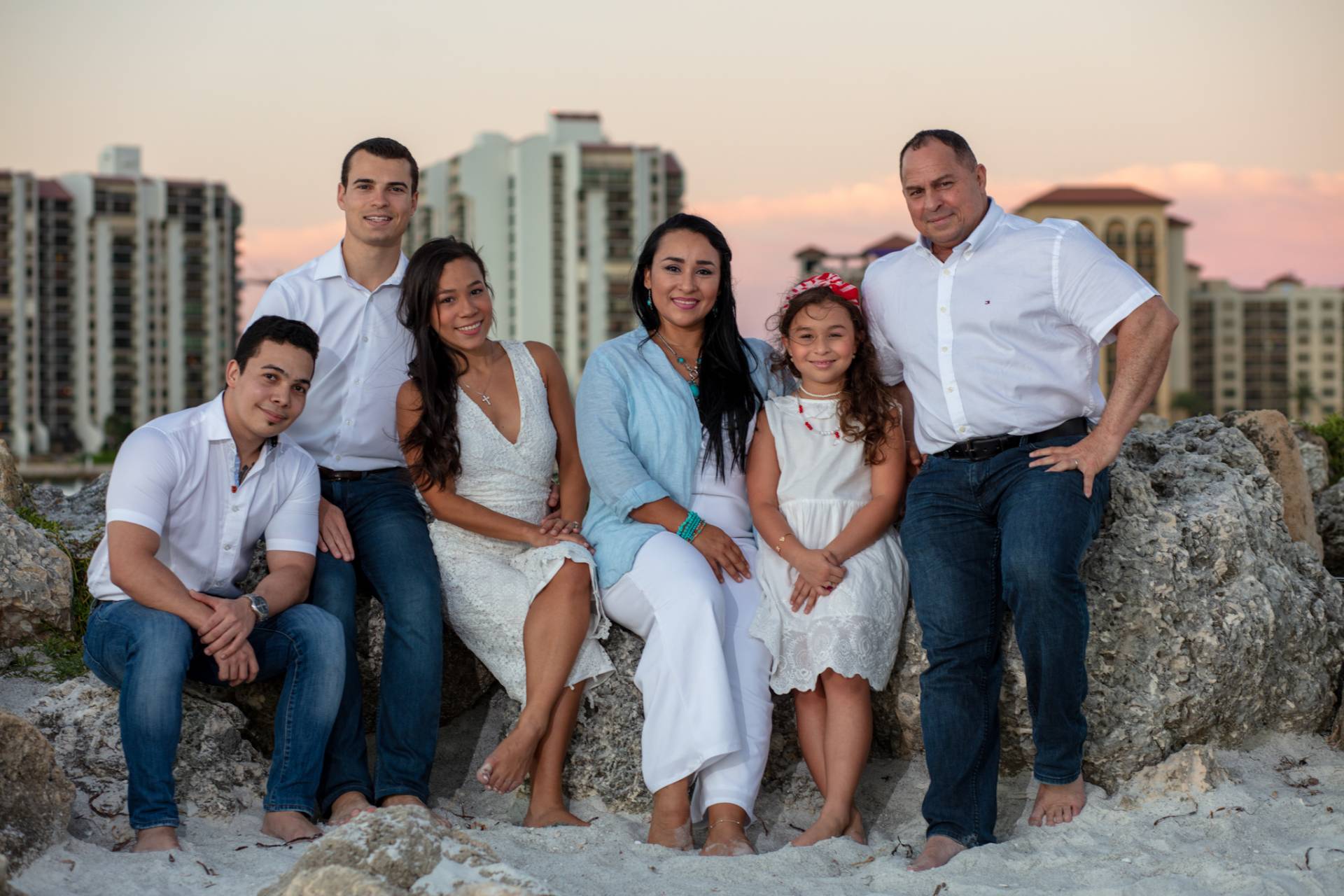 family of 6 sitting on a pile of rocks on the beach at sunset
