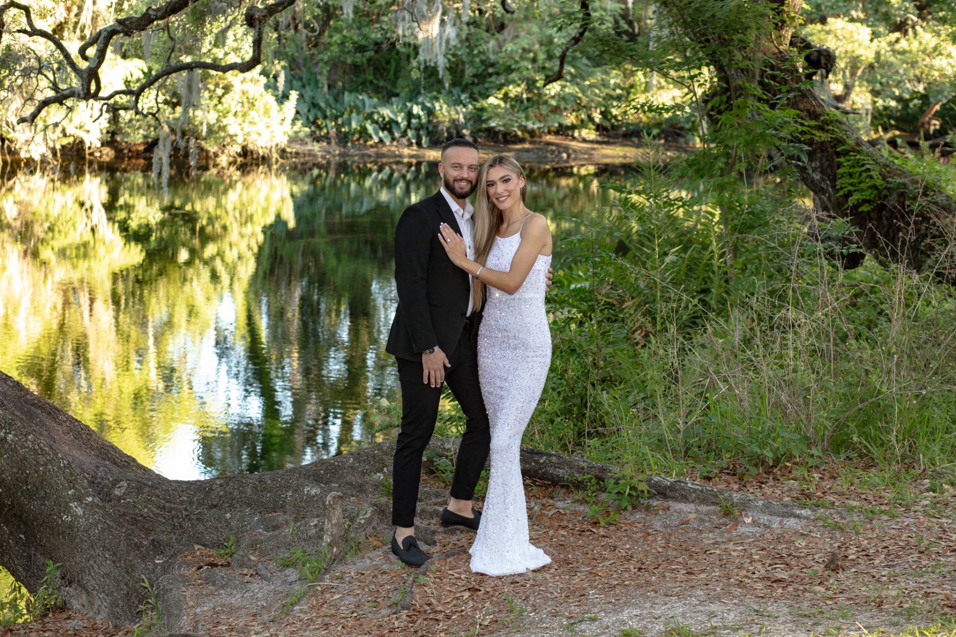 bride and groom posing by the river in the grass surrounded by trees