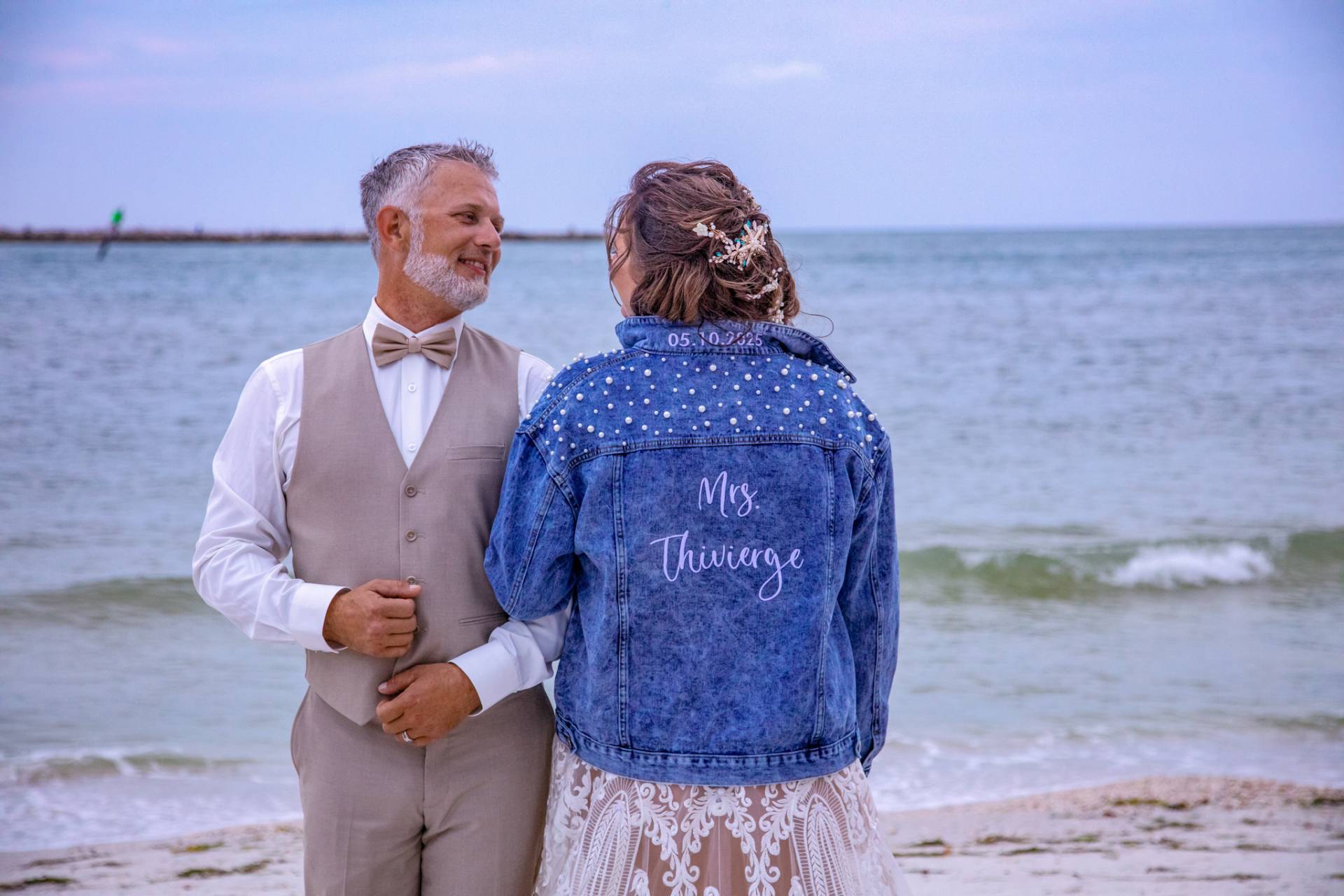 bride in her custom denim jacket looking at the groom on the beach