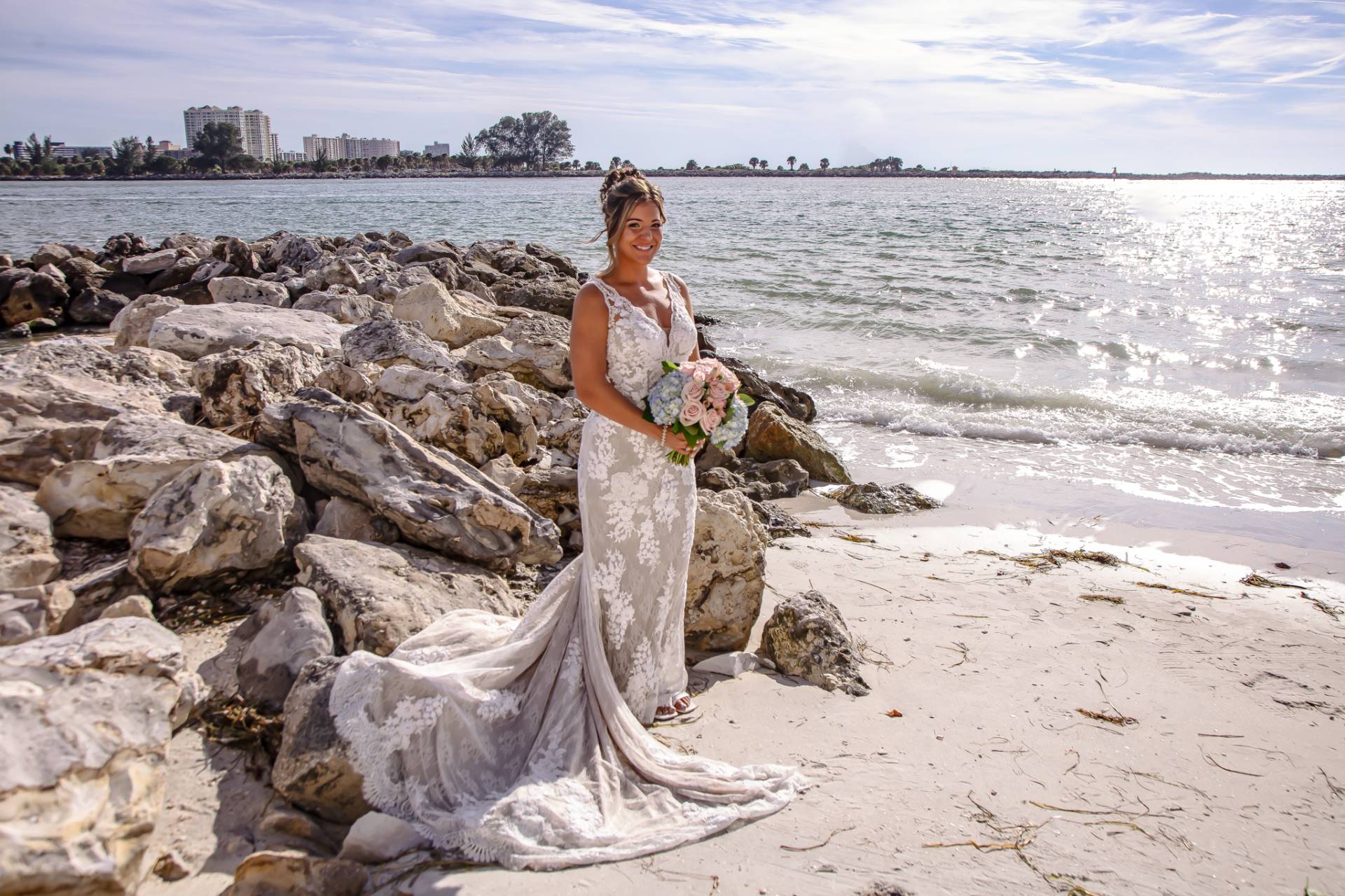 bride standing on the beach near some rocks in her wedding dress