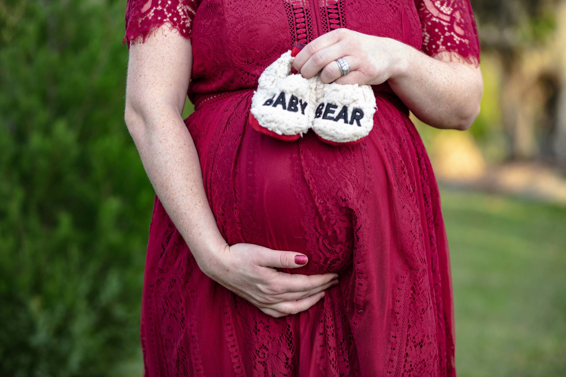 momma holding baby bear slippers on her pregnant belly in a red dress