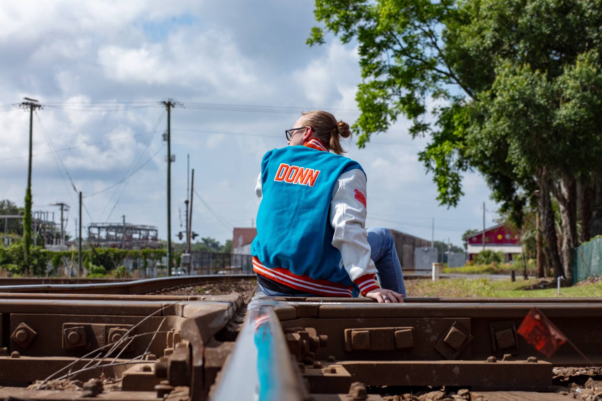 graduate sitting on the train tracks with custom jacket on