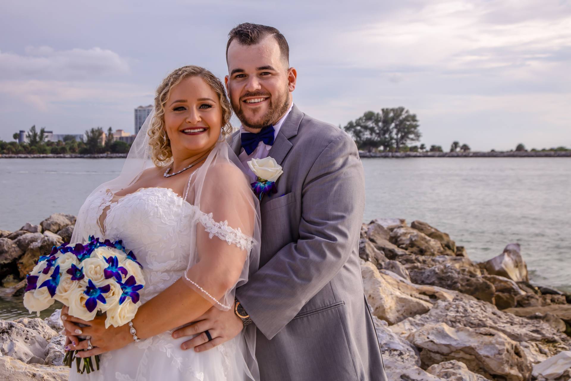 bride and groom standing on some rocks on the beach