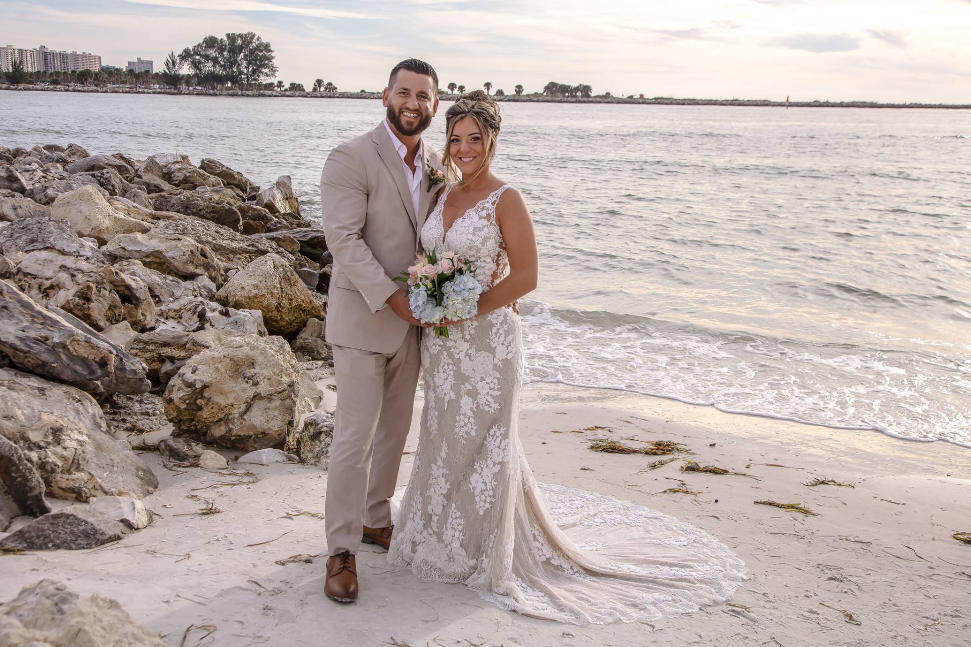 bride and groom standing on the beach near some rocks