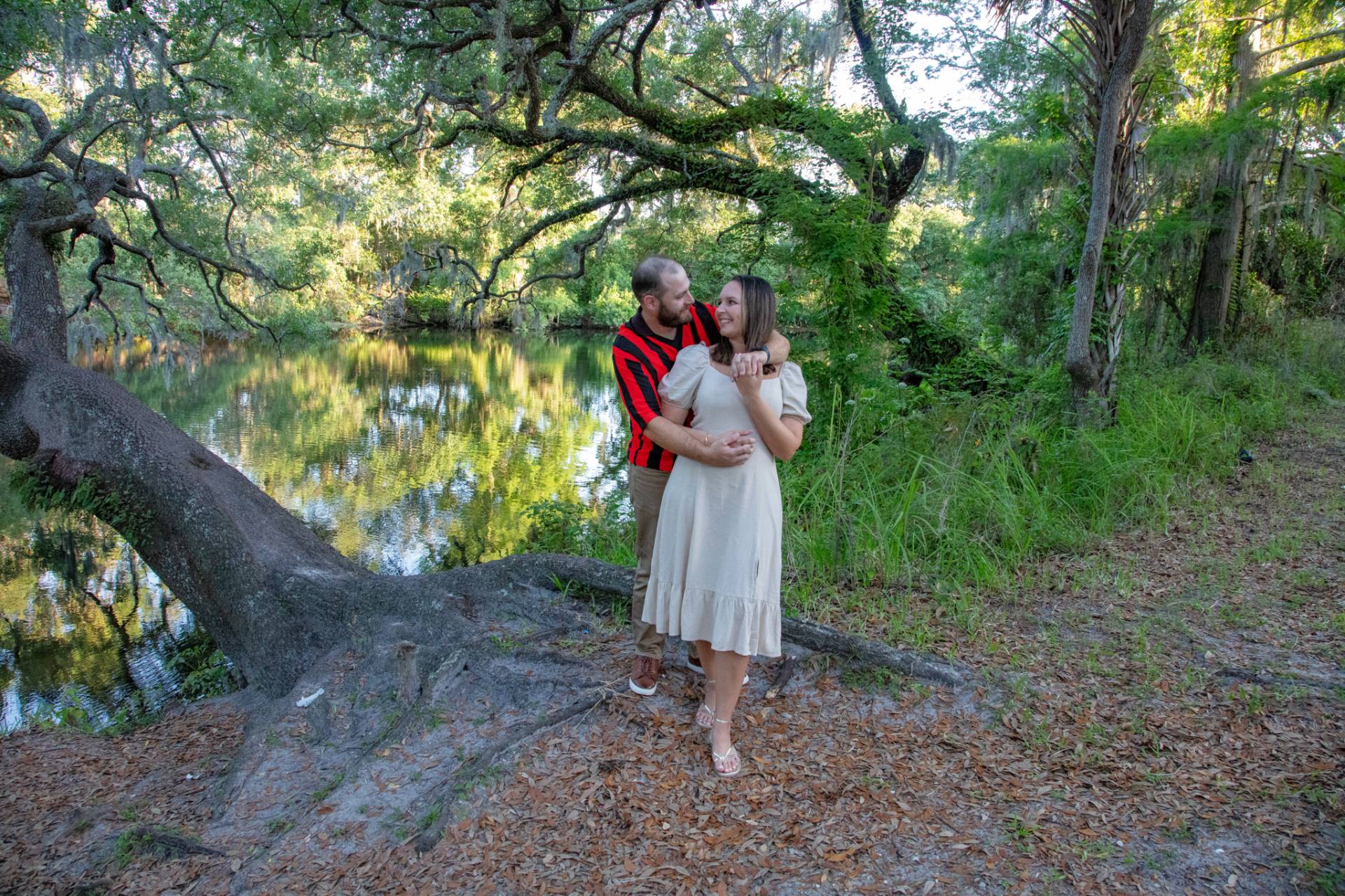 man and woman hanging by a tree with river in the background