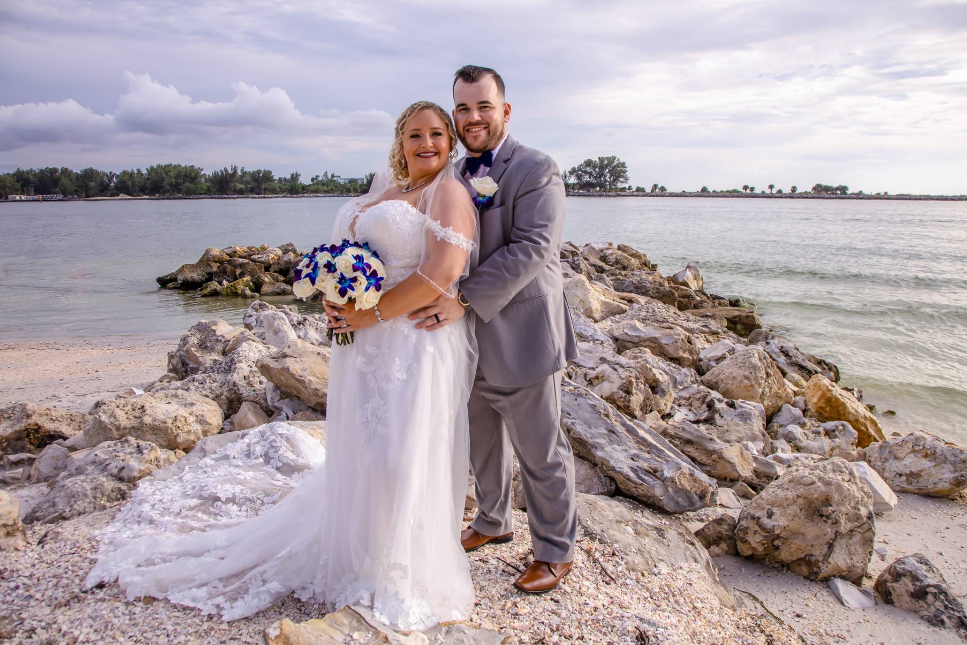 bride and groom standing on some rocks on the beach