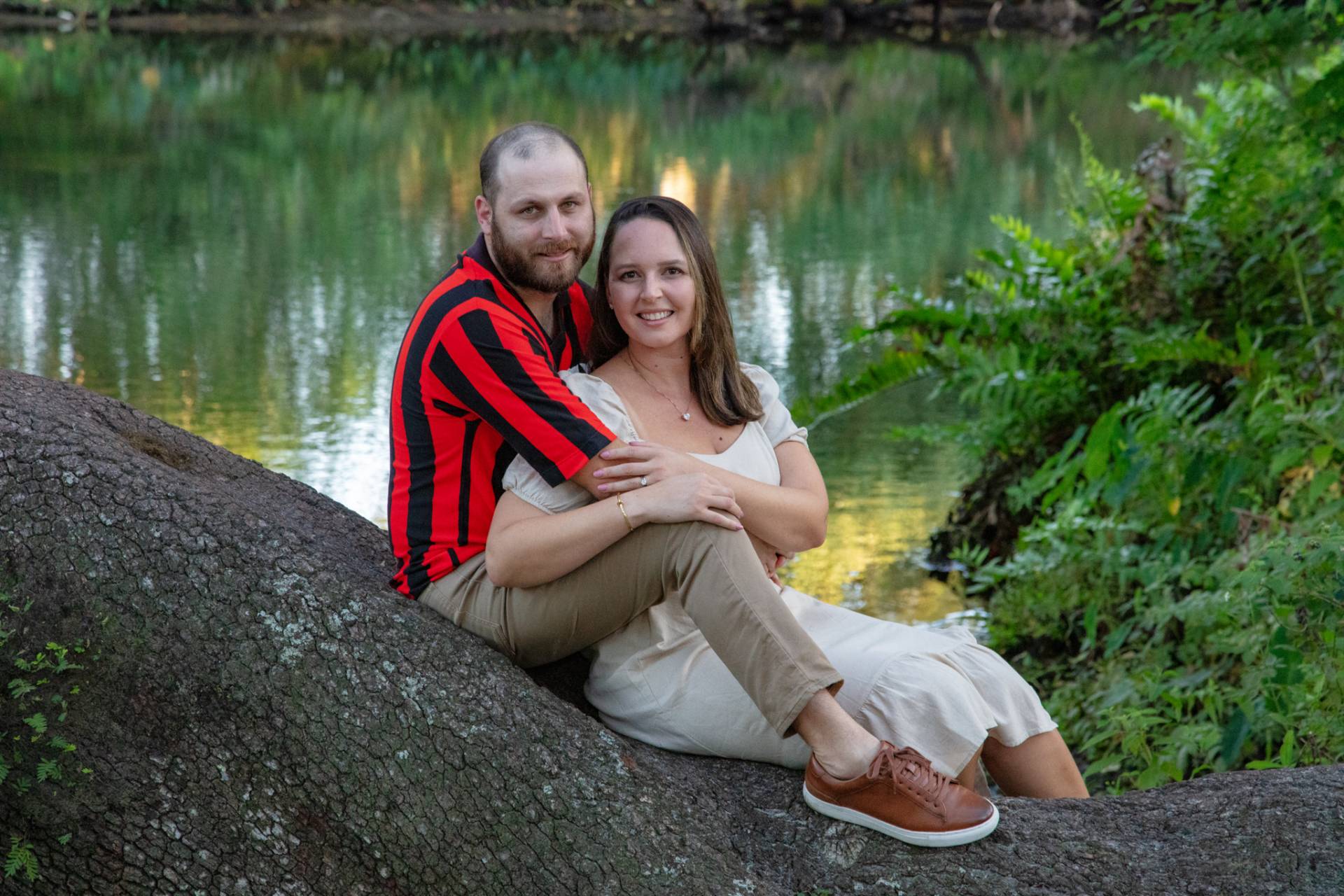 man and woman sitting on a tree trunk with the river in the background