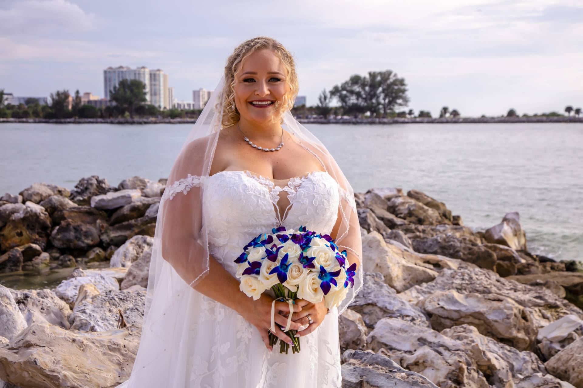 bride standing on some rocks on the beach in her wedding dress